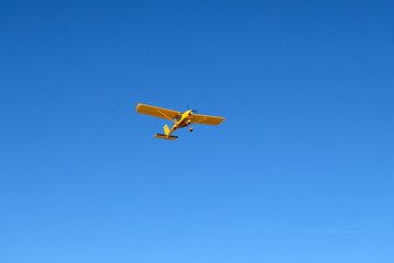 Naklejka na ściany i meble A small yellow airplane ia in the blue sky.