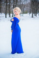 Winter holidays, celebration and people concept - young sexy woman in elegant blue dress over snowy forest background