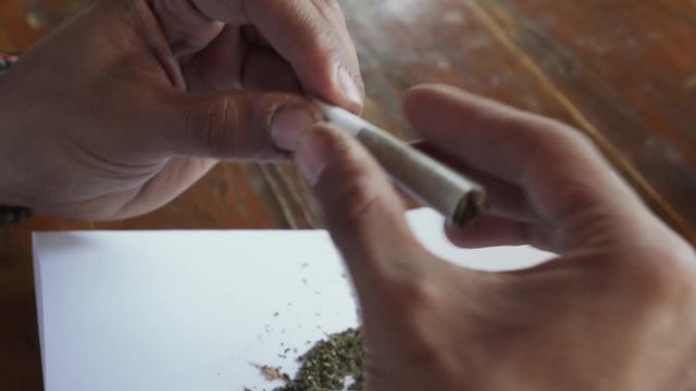 Close up man hands rolling marijuana joint and licking cigarette paper