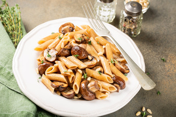 Vegetarian pasta penne with mushroom and pine nuts on kitchen table background. Healthy italian food concept.