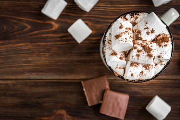Mug with hot drink with marshmallow, chocolate bars and knitted scarf on dark wooden background