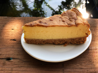 New York  cheese cake in white dish on the wooden table with sunlight . Homemade bakery.