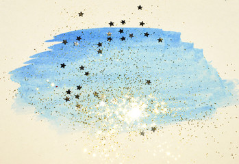 Fototapeta na wymiar Golden glitter and glittering stars on abstract blue watercolor splash in vintage nostalgic colors.