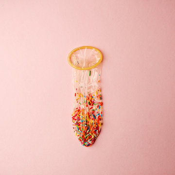 a condom full of nonpareils of many colors on pink background, love saint valentine concept