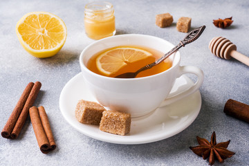 Cup of tea with lemon and brown sugar, cinnamon and anise on the table.