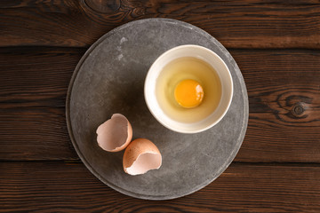 plate with raw broken egg, shell on concrete slab