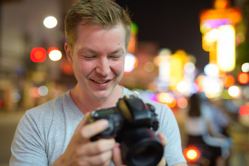 Face of young happy tourist man checking camera in the streets of Chinatown at night