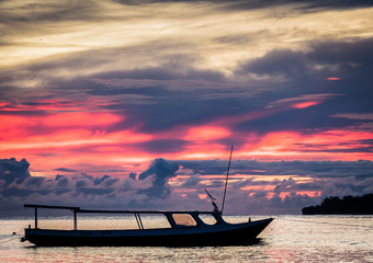 Amazing pink sky and clouds over the ocean with a silhouette of a boat