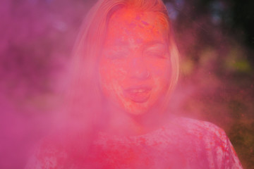 Attractive blonde woman having fun with exploding pink dry powder celebrating Holi festival