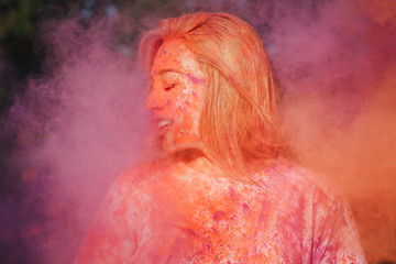 Pretty blonde girl having fun with exploding orange and pink dry powder celebrating Holi festival