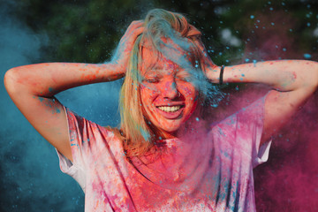 Emotional blonde woman having fun with exploding blue and pink dry powder celebrating Holi festival
