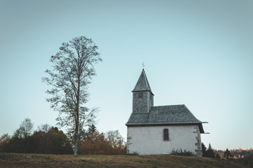 tiny church on mount with tree in front of blue sky