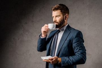 Handsome businessman drinking coffee and holding saucer