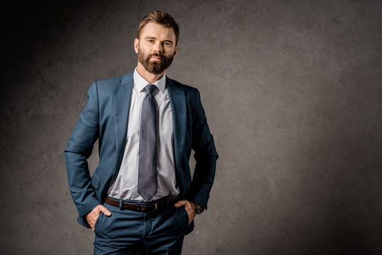 handsome bearded businessman standing in formalwear with hands in pockets