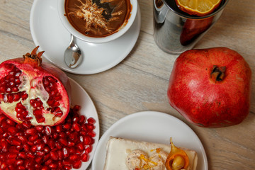 Homemade cake, pomegranate and coffee in a white cup on a wooden vintage table