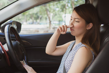 Young woman holding her nose because of bad smell in car.