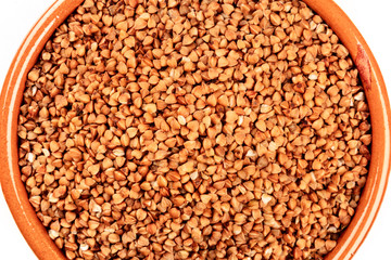 A closeup photo of dry buckwheat in an earthenware bowl, shot from the top, isolated on a white background