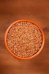 A photo of dry buckwheat in an earthenware bowl, shot from above on a dark rustic wooden background with copy space