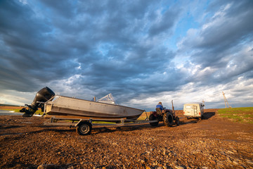 Fototapeta premium Rural landscape with car, tractor and boat. Blue thunderstorm sky in yakutian village, Yakutia, Siberia. These vehicles are the most necessary thing in the villages.