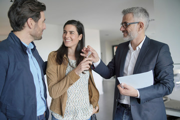  Real-estate agent handing over keys to new home owners in contemporary house