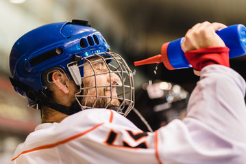 hockey player drinks from a bottle and then pours water over his face