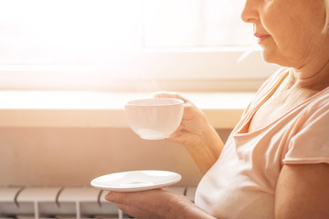 Close up of a woman hands holding a hot coffee cup in winter near a window at home