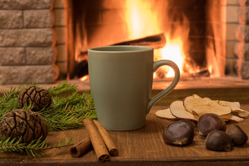 Cozy scene near fireplace with mug of hot chocolate , tangarine, cones and cinnamon sricks .