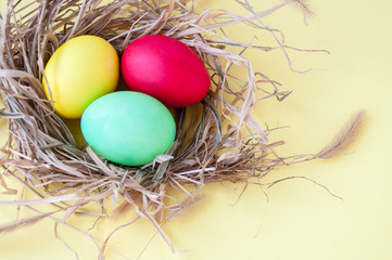 Easter multicolored eggs in a nest on a yellow background