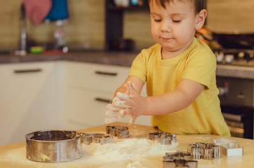 Sweet little cute child boy is learning how to make a cake, in the home kitchen. Concept of family...