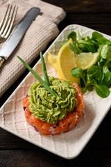 Salmon tartare with guacamole, on dark background.