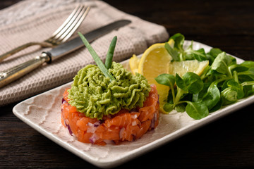 Salmon tartare with guacamole, on dark background.