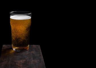 Glass of lager beer with foam and bubbles on vintage wooden board on black background. Space for text