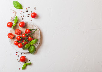 Naklejka na ściany i meble Organic Mini San Marzano Tomatoes on the Vine with basil and pepper on chopping board on white kitchen background. Space for text