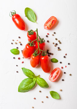 Organic Mini San Marzano Tomatoes on the Vine with basil and pepper on white kitchen background