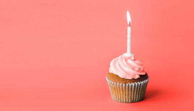 holiday, celebration, greeting and party concept - birthday cupcake with one burning candle in trendy color of the year 2019 living coral