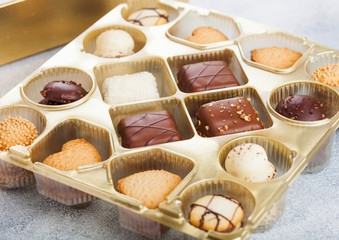 Luxury belgian chocolate and biscuit cookies selection in original golden tray and white kitchen table background.