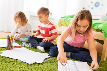 Naklejka premium childhood, leisure and people concept - happy kids with paper, crayons and washi tape making crafts at home