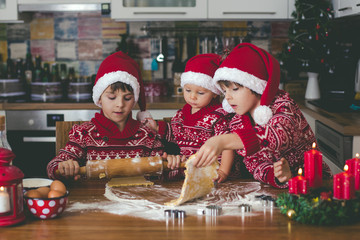 Sweet toddler child and his older brother, boys, helping mommy preparing Christmas cookies at home .