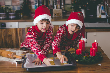 Sweet toddler child and his older brother, boys, helping mommy preparing Christmas cookies at home .