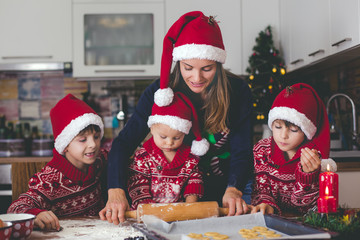 Sweet toddler child and his older brother, boys, helping mommy preparing Christmas cookies at home .