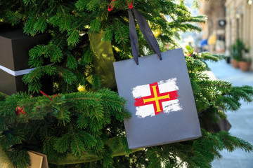 Guernsey flag printed on a Christmas shopping bag. Close up of a shopping bag as a decoration on a Xmas tree on a street. New Year or Christmas shopping, local market sale and deals concept.