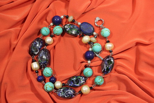 Necklace made of semi-precious natural stones - lapis lazuli, turquoise, pearls and glass beads on a pink background.