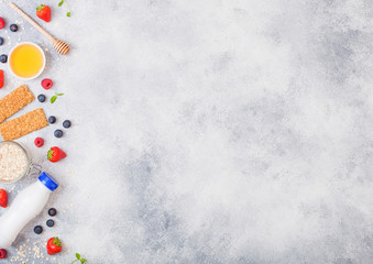 Organic cereal granola bar with berries with honey spoon and jar of oats and bottle of milk drink on stone table background. Space for text.Strawberry, raspberry and blueberry with almond nuts.