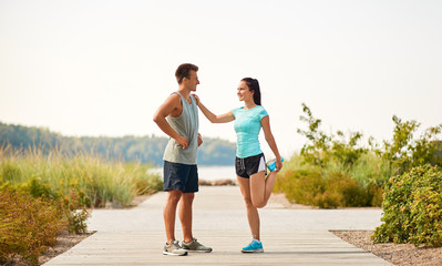 fitness, sport and lifestyle concept - smiling couple stretching legs on beach before training