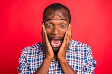Close-up portrait of nice handsome attractive scared afraid guy wearing checked shirt holding cheeks in hands opened mouth isolated over bright vivid shine red background