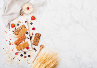 Fototapeta na wymiar Organic cereal granola bar with berries on marble board with honey spoon and jar of oats and linen towel on marble background. Space for text.Top view