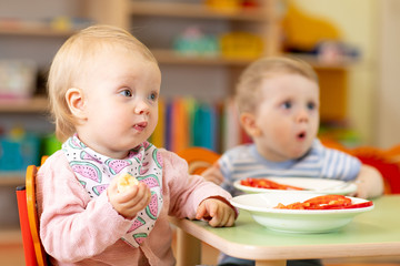 children girl and boy eating healthy food in nursery or kindergarten