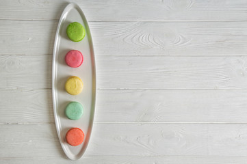 Close up. Flat lay. Colorful pastry french macarons lined up in a row on white plate. Copy space.