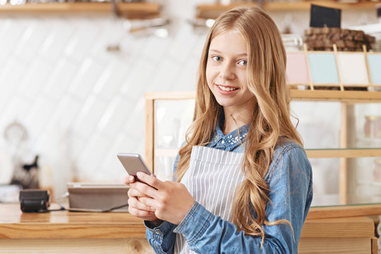 Friendly looking girl with smartphone smiling into camera - Powered by Adobe