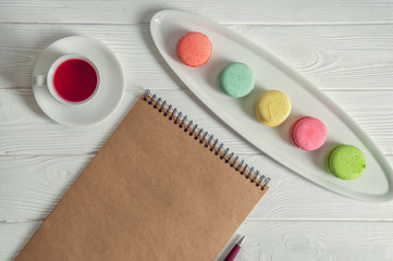 Flat lay. Close up. Provence breakfast. Bright colorful macarons, brown vintage notebook, a pen, a cup of berry tea. Copy space.